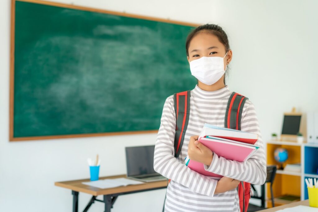 Early Teen Asian School Girl Wearing A Mask in Front of a Blackboard