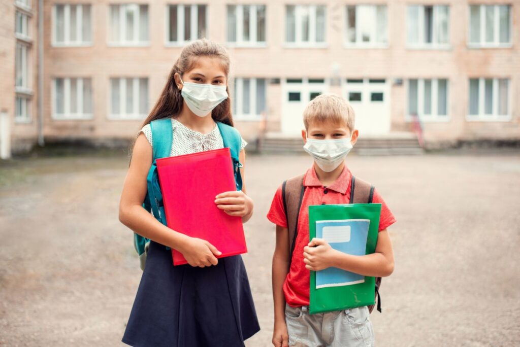 Preteen Sister and Brother Wearing Masks Holding Books in the Schoolyard